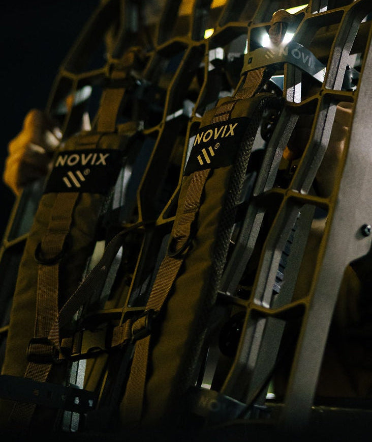 A person at night holding up a large, illuminated Novox tactical display board filled with multiple small LED light modules. The Novox brand name is clearly visible on the display and on the person's sleeve.